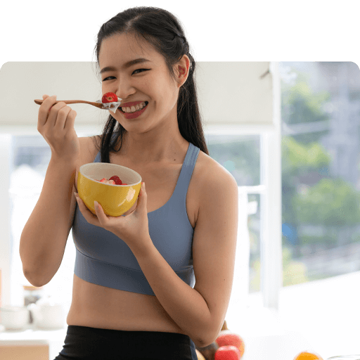 Smiling woman in activewear holding a bowl of fruit, promoting healthy habits and lifestyle choices for clients in a coaching context.